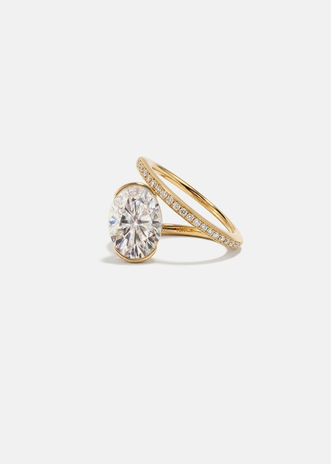 Oval cut moissanite bezel set engagement ring on a spiral pave band in yellow gold