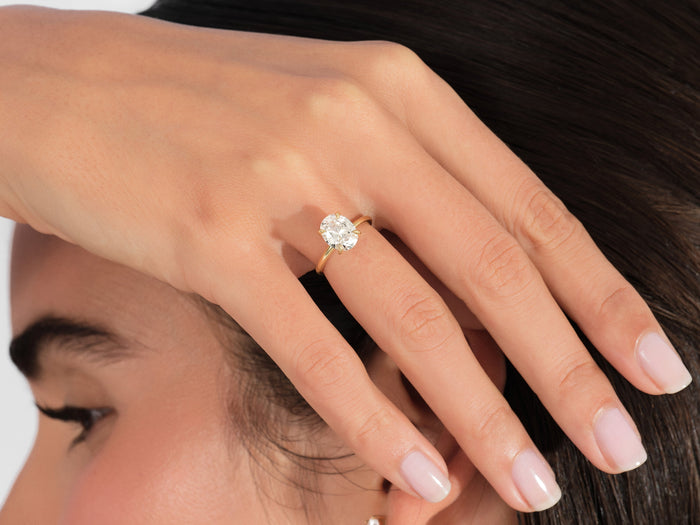 Oval lab grown diamond solitaire engagement ring worn on the hand resting against the hair