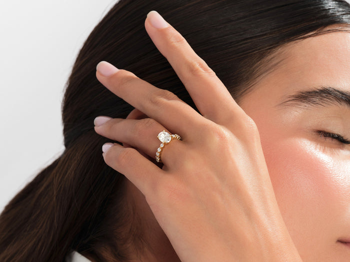 Oval lab grown diamond side stone ring in yellow gold worn on the hand in the hair