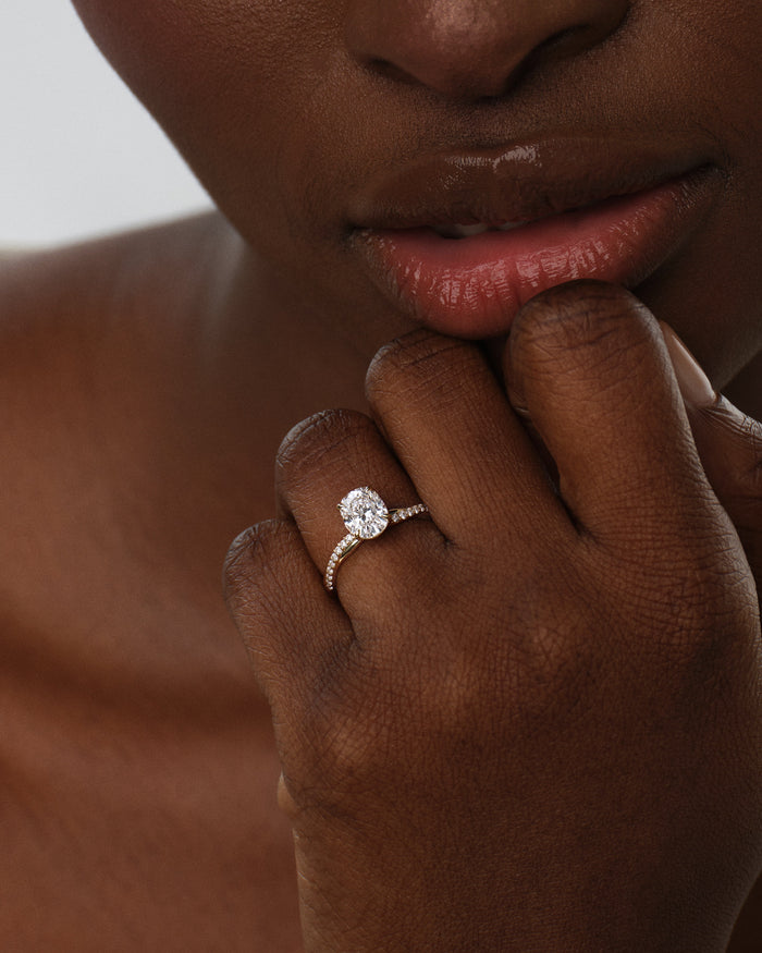 Oval moissanite infinity twist pave engagement ring worn on the hand near the lips