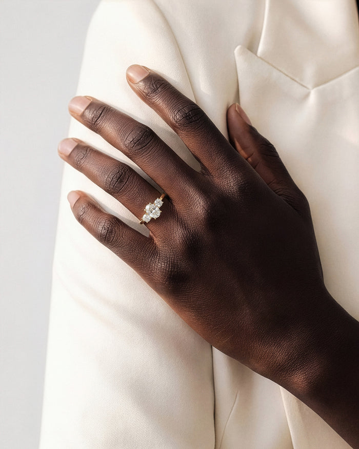 Oval lab grown diamond trilogy ring in yellow gold worn on the hand across a cream jacket