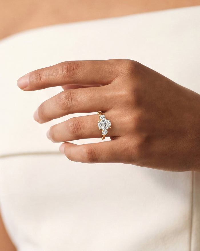 Oval moissanite three stone ring in yellow gold worn on the ring finger, hand raised