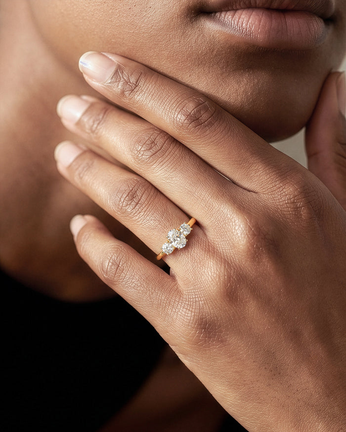 Oval moissanite three stone ring in yellow gold worn on the ring finger, hand at the chin