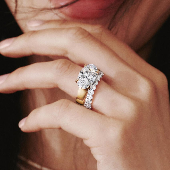 Wide flat gold band with an oval moissanite worn on the hand