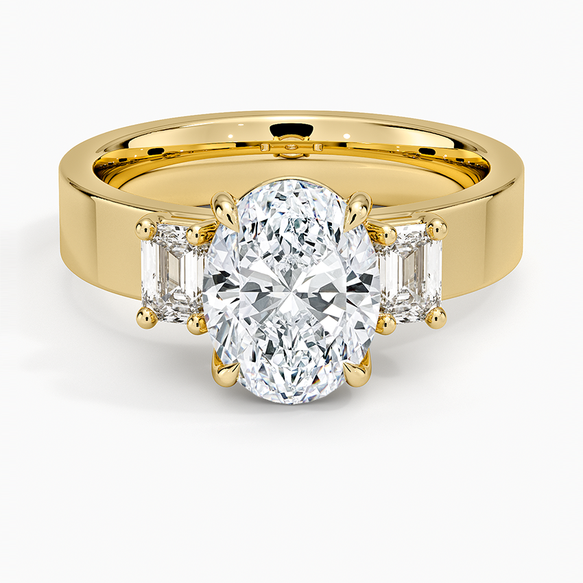 Oval moissanite with emerald cut side stones on a wide flat yellow gold band, top view