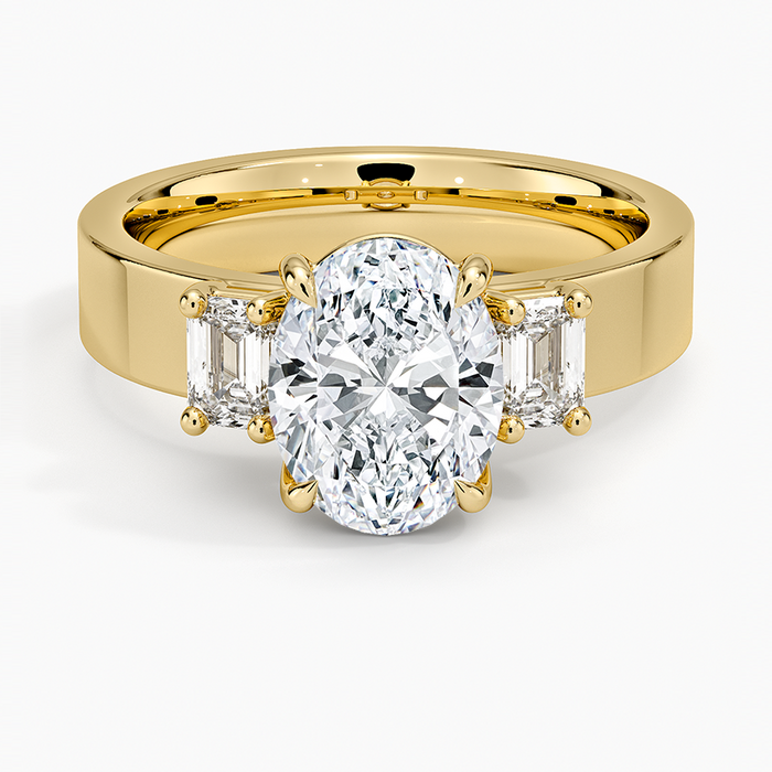 Oval moissanite with emerald cut side stones on a wide flat yellow gold band, top view