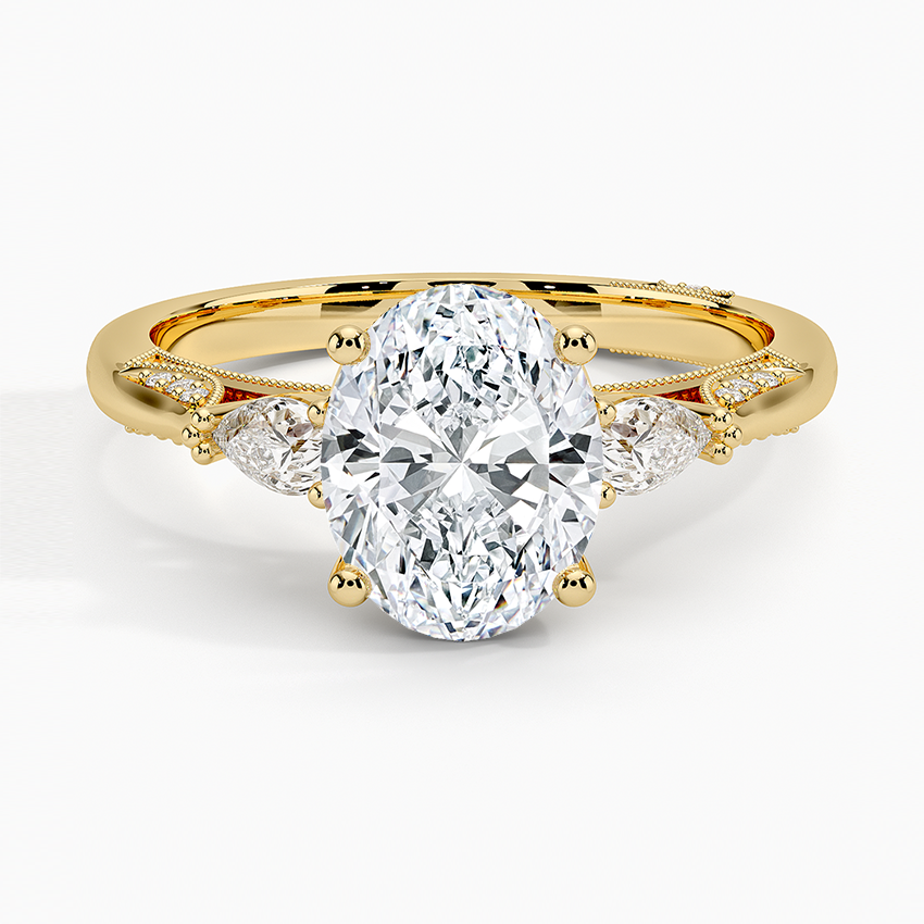 Oval moissanite with pear side stones and milgrain scroll wings in yellow gold, top view