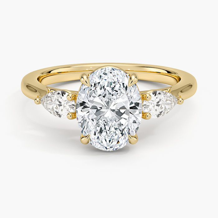 Oval moissanite with two outward facing pear side stones in yellow gold, top view