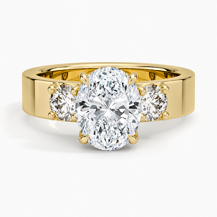 Oval moissanite three stone ring with round side stones on a wide flat yellow gold band, top view