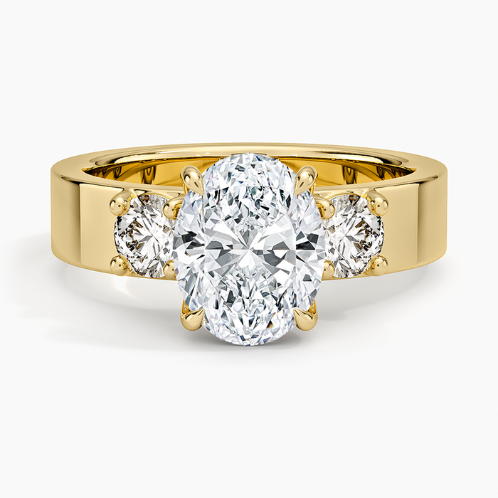 Oval moissanite three stone ring with round side stones on a wide flat yellow gold band, top view