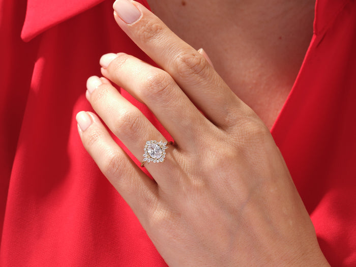 Vintage oval moissanite halo ring in rose gold worn on the hand against a red top