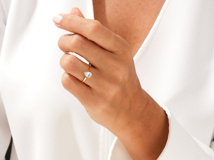 Pear cut lab grown diamond minimalist bezel ring in yellow gold on a hand resting on a white shirt