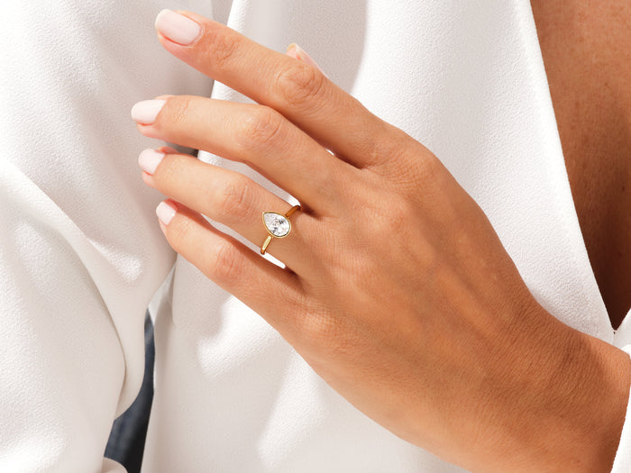 Pear shaped lab grown diamond teardrop bezel ring in yellow gold worn on the ring finger
