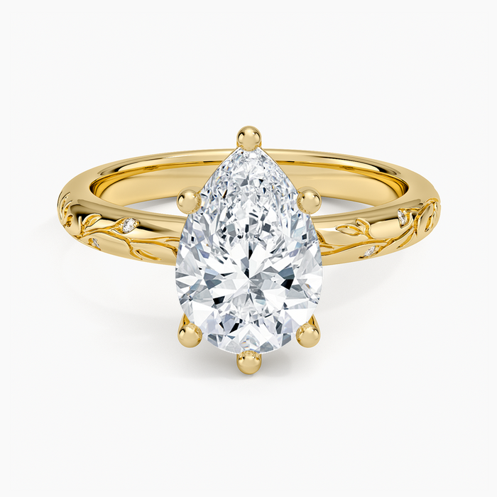 Pear cut moissanite on a slim band with a sculpted vine and leaf shoulders in yellow gold, top view
