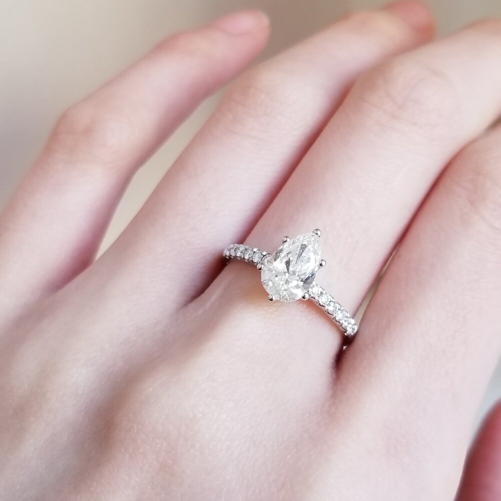 Pear cut moissanite four claw engagement ring on a French pave band in white gold