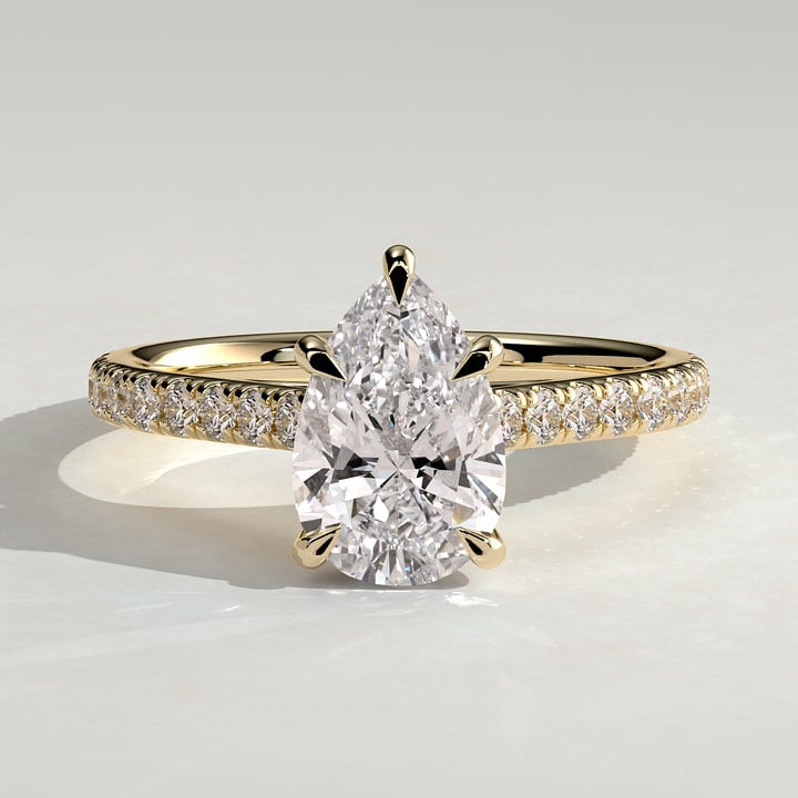 Pear cut moissanite five claw engagement ring on a fine pave yellow gold band