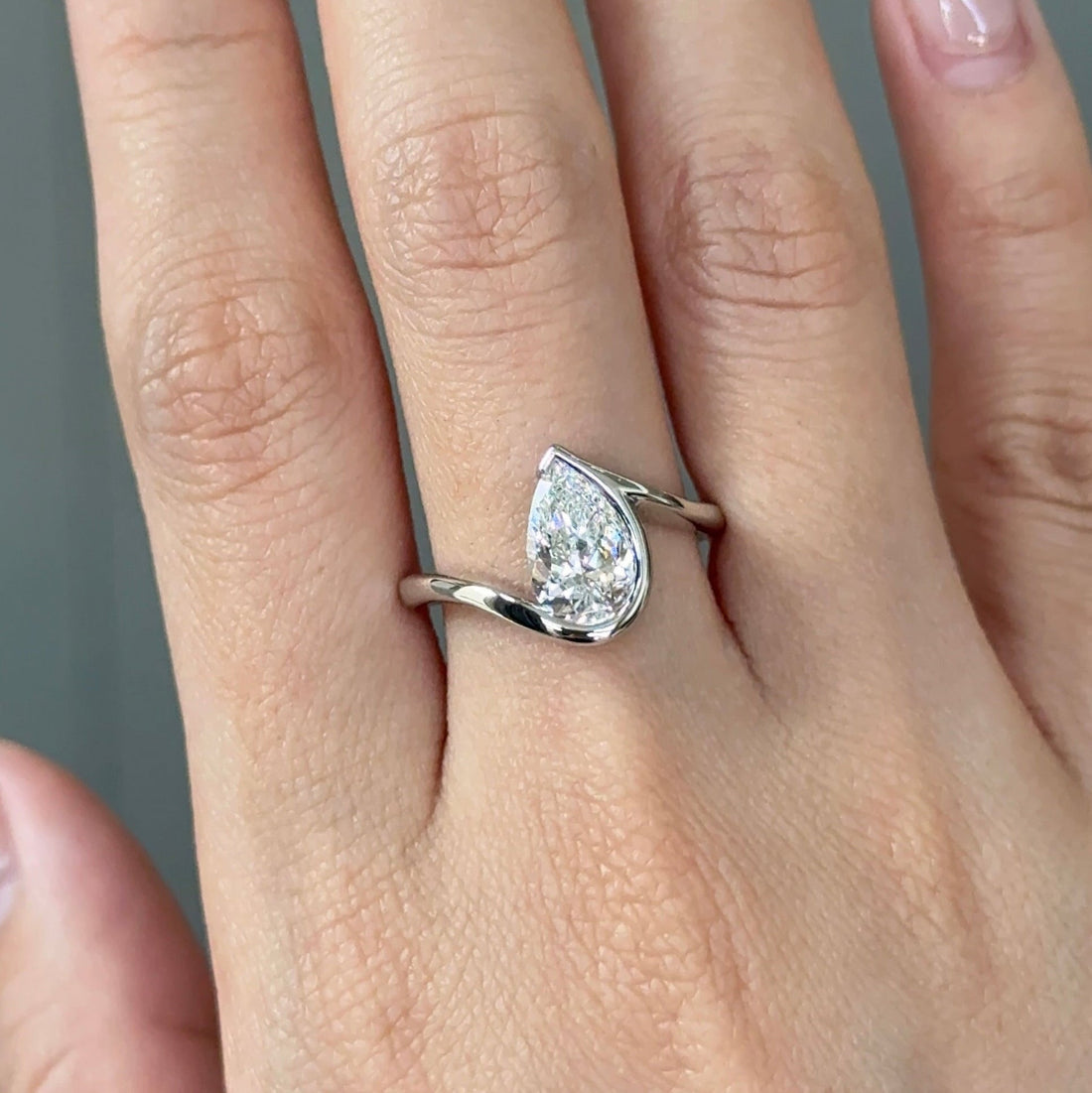 Pear cut moissanite half bezel engagement ring on a bypass shank in white gold
