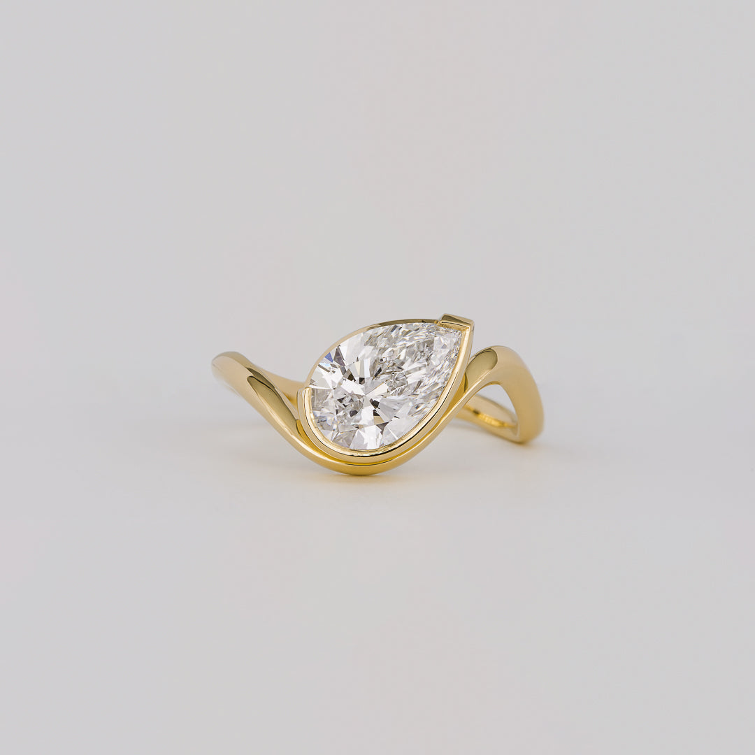East west pear cut moissanite half bezel engagement ring on a curved yellow gold band