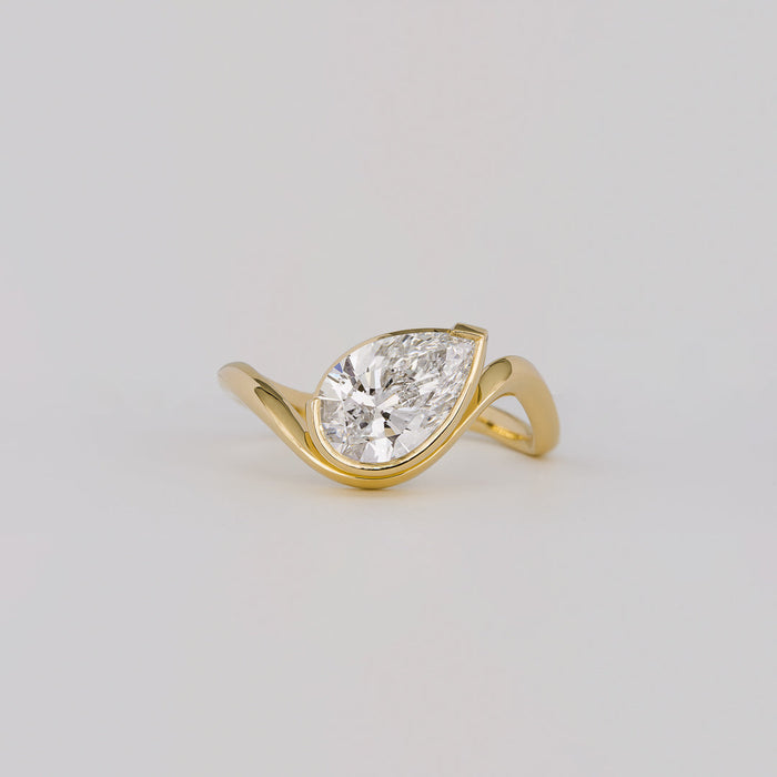 East west pear cut moissanite half bezel engagement ring on a curved yellow gold band