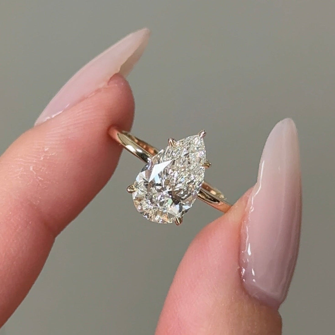 Pear cut moissanite hidden halo engagement ring on a knife edge yellow gold band