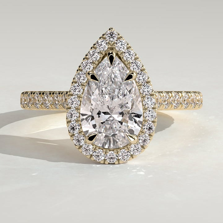 Pear cut moissanite halo engagement ring on a pave yellow gold band in yellow gold