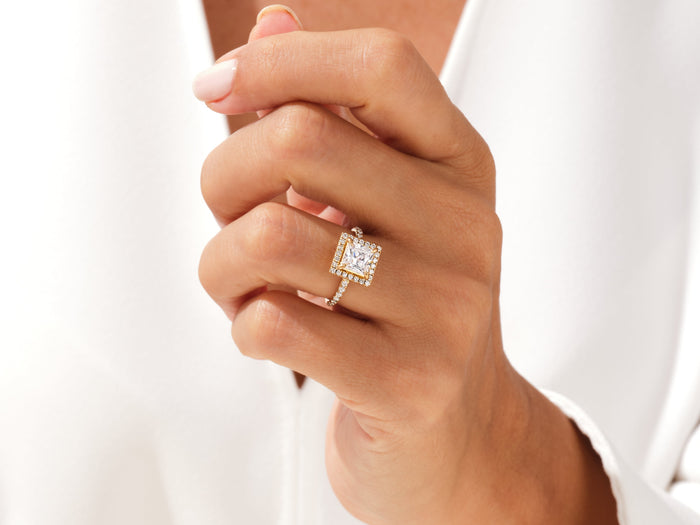 Princess moissanite halo ring in yellow gold on a hand held close to the chest