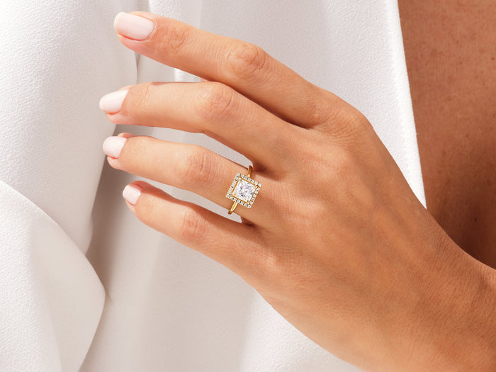 Square princess moissanite halo ring in yellow gold worn on the ring finger