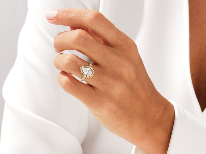 Pear lab grown diamond halo engagement ring with pave band worn on the hand against a white shirt