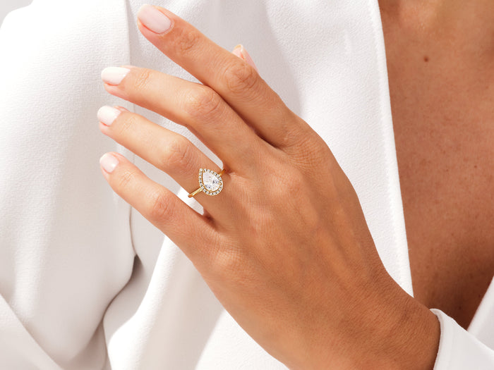 Pear shaped lab grown diamond halo ring in yellow gold worn on the hand against a white shirt