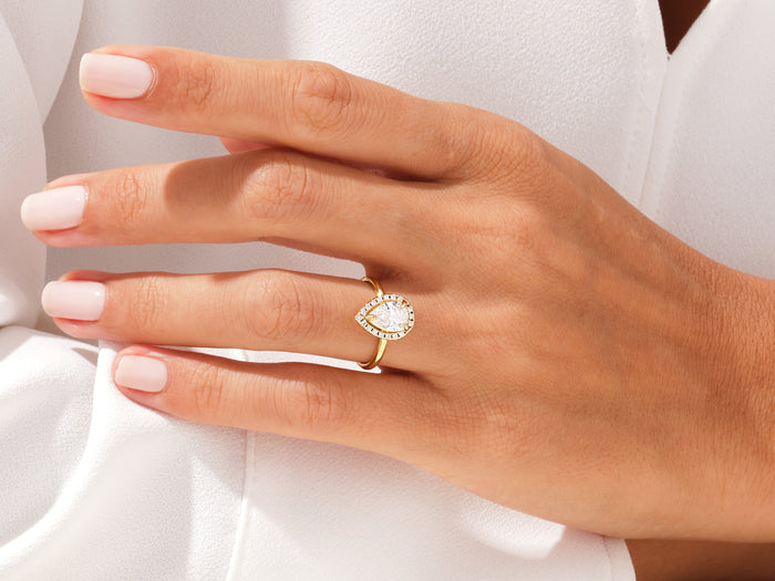 Pear cut lab grown diamond halo ring in yellow gold worn on an outstretched hand