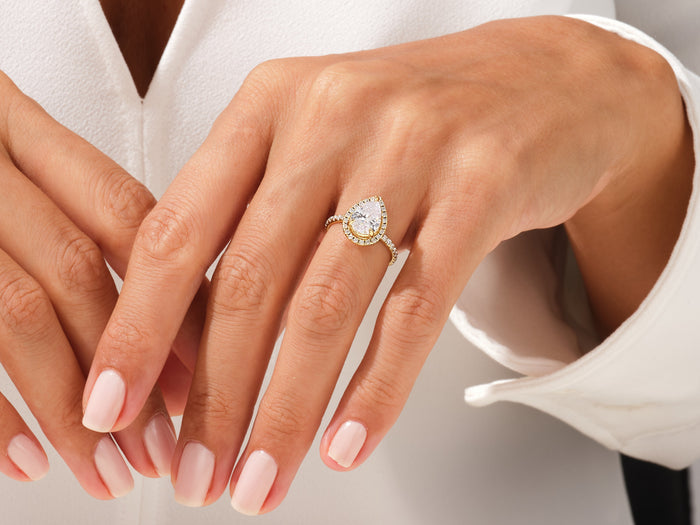 Pear lab grown diamond halo ring in yellow gold worn on the hand with a white shirt cuff