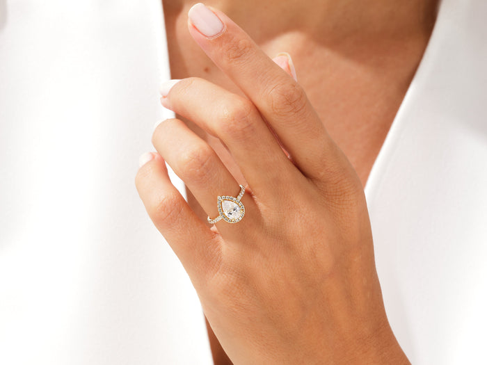 Pear shaped lab grown diamond teardrop halo ring in yellow gold on a hand raised to the collar