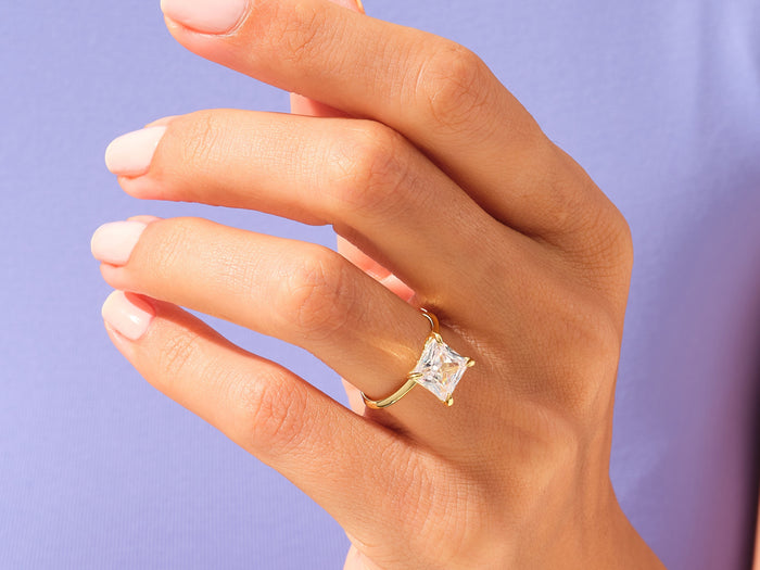 Princess cut lab grown diamond statement solitaire worn on the hand against a lilac background