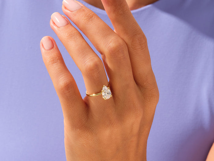 Pear lab grown diamond statement ring in yellow gold worn on a hand against a lilac top