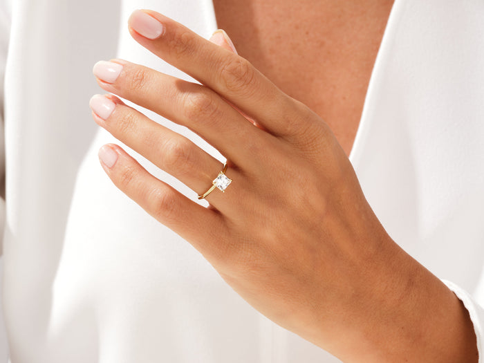 Princess cut lab grown diamond dainty solitaire on a hand held at the chest
