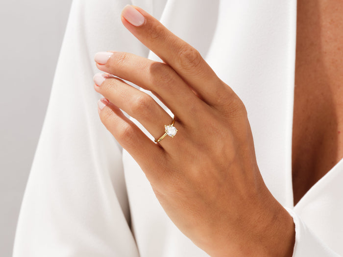 Pear shaped lab grown diamond knife edge ring in yellow gold on a hand resting on white fabric