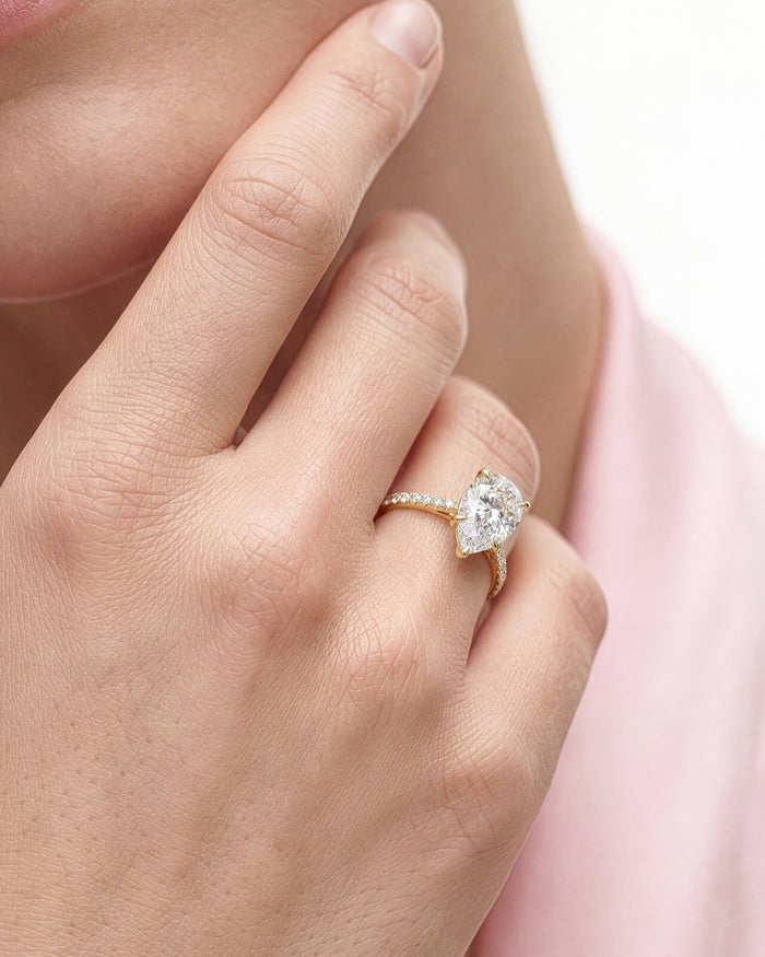Large pear lab grown diamond ring in yellow gold, close view on a hand against pink fabric