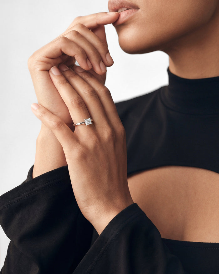 Princess cut lab grown diamond solitaire ring in white gold worn on the hand near the lips
