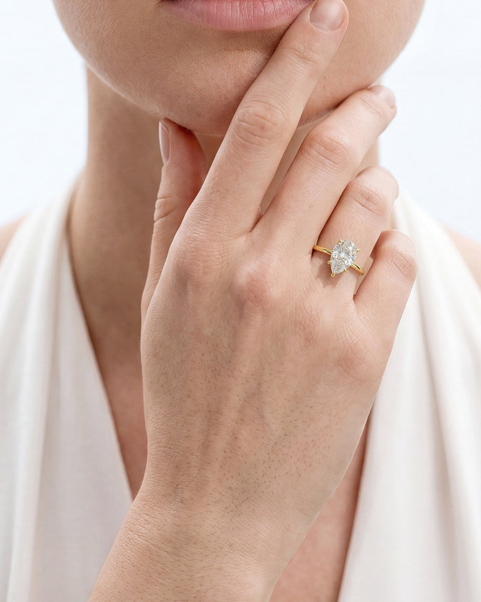 Pear lab grown diamond statement solitaire in yellow gold worn on the hand at the chin