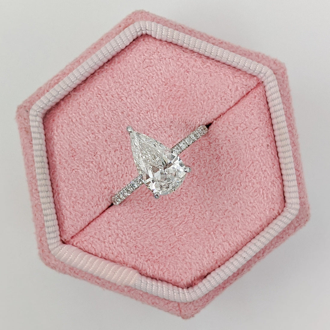 Pear cut moissanite three claw solitaire engagement ring on a pave band in white gold