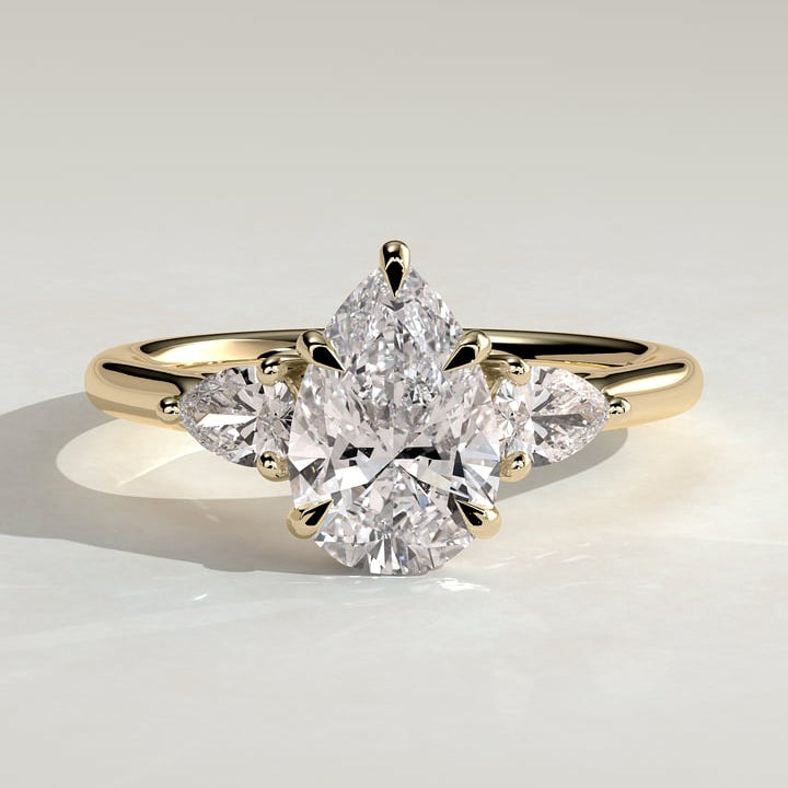 Pear cut moissanite three stone engagement ring with trillion side stones in yellow gold
