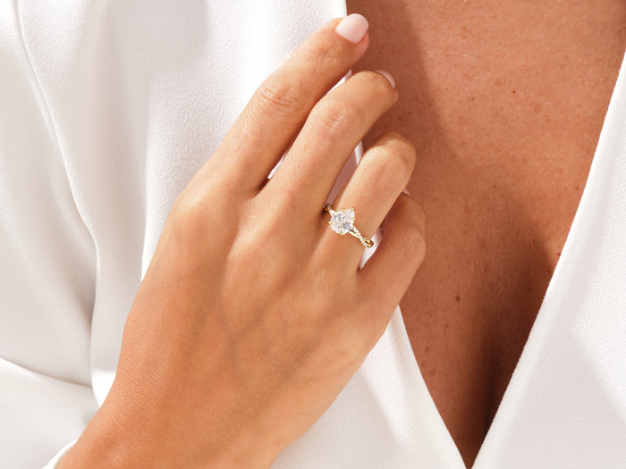 Pear lab grown diamond twisted engagement ring in yellow gold worn on the hand against a white blouse