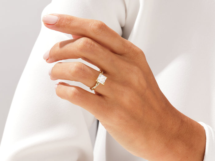 Princess cut lab grown diamond infinity twist ring in yellow gold worn on the hand resting on white fabric