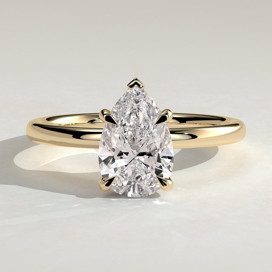 Pear cut moissanite V claw solitaire engagement ring on a domed yellow gold band