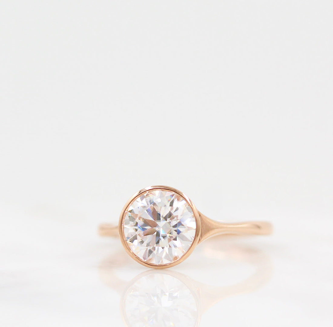 Round brilliant moissanite bezel engagement ring on a pinched tapered rose gold band