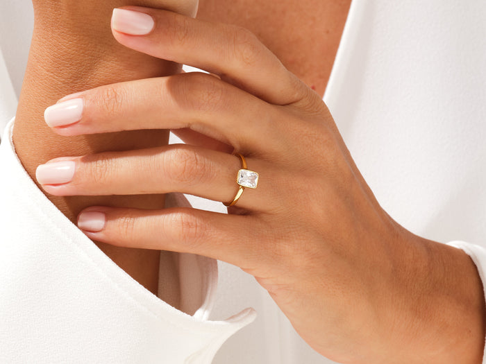 Elongated radiant moissanite bezel engagement ring in yellow gold worn on the hand
