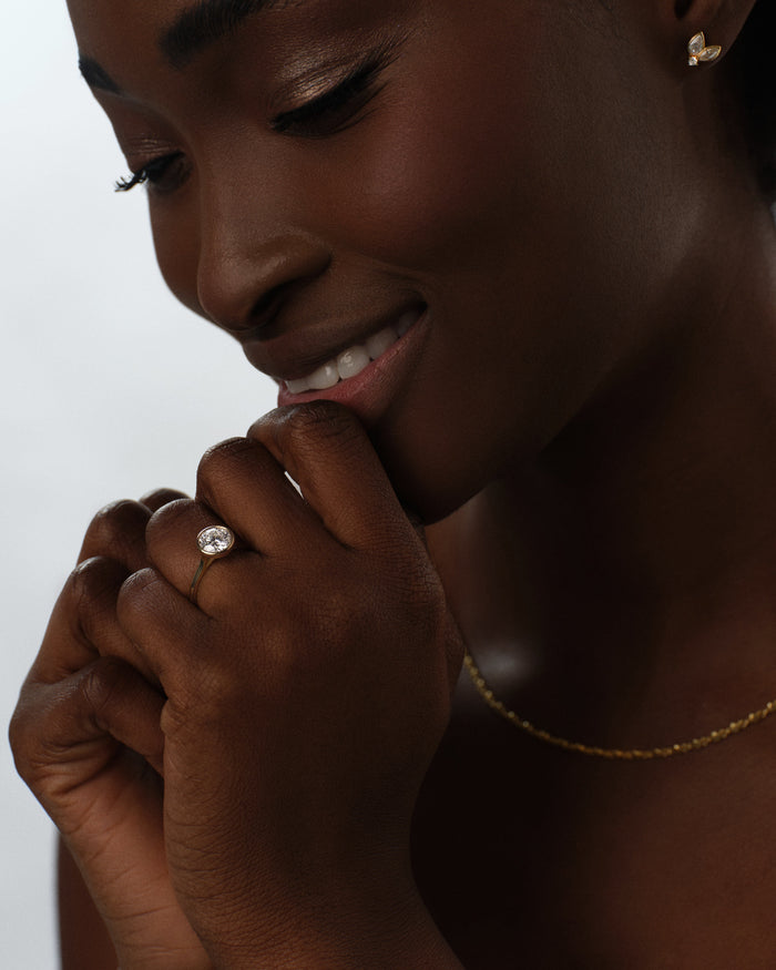 Round lab grown diamond full bezel engagement ring in yellow gold worn with the hand raised to the lips