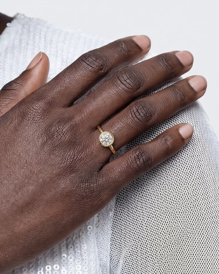 Round lab grown diamond bezel solitaire in yellow gold worn on the hand over a sequin dress