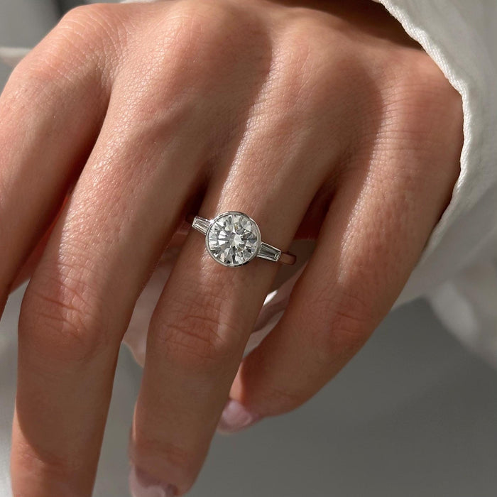 Round moissanite bezel three stone engagement ring with tapered baguettes in white gold, view 2