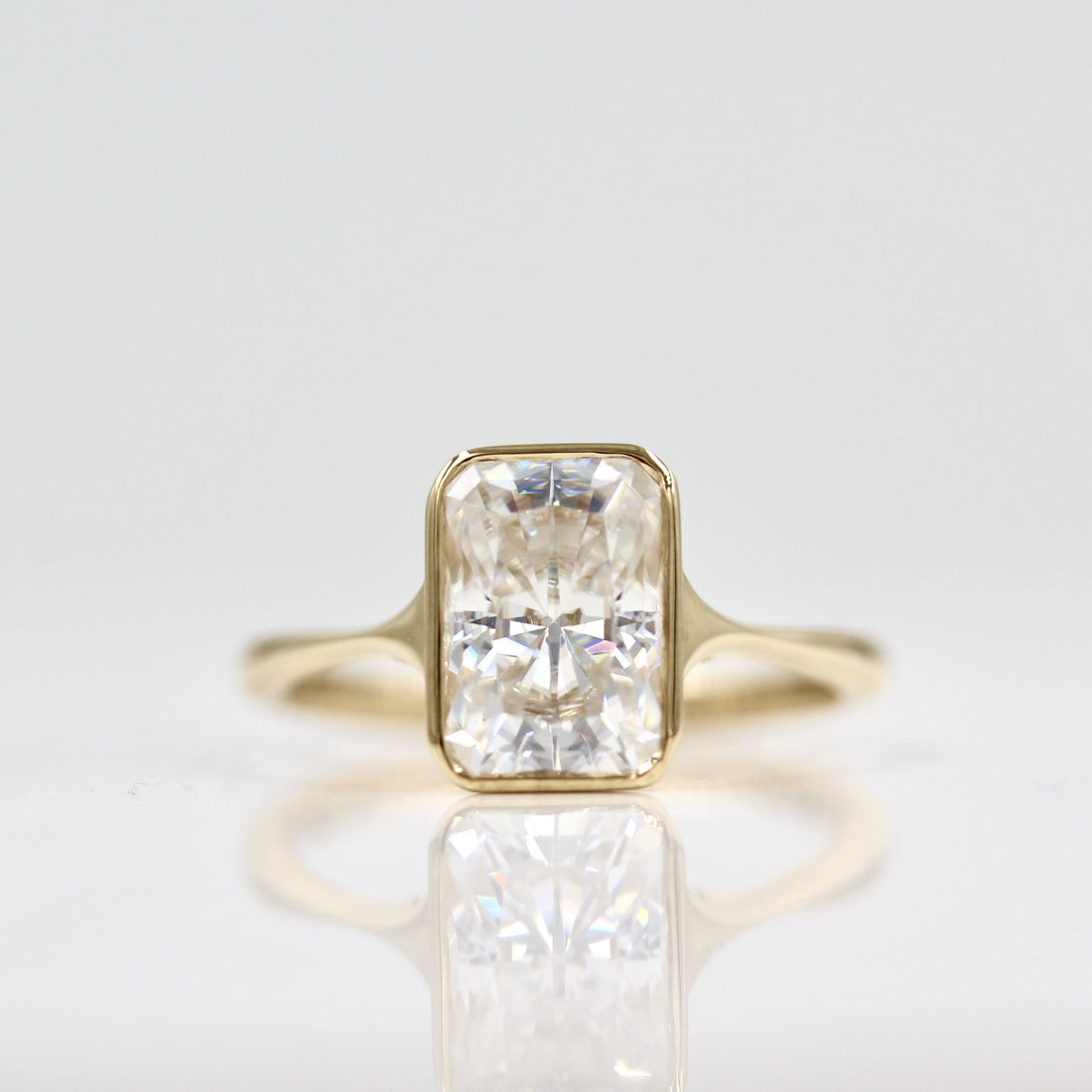 Radiant cut moissanite bezel engagement ring on a pinched tapered yellow gold band